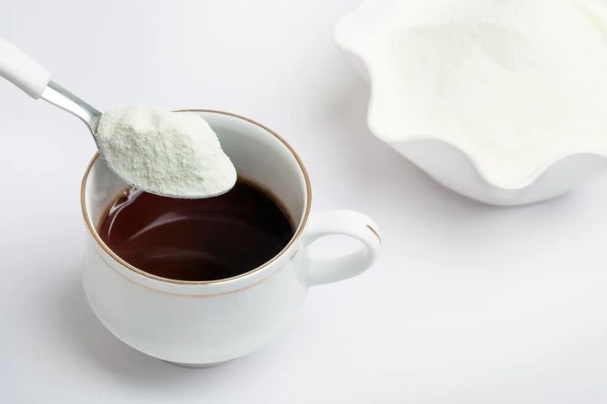 Fat filled milk powder in a spoon above a cup of coffeee